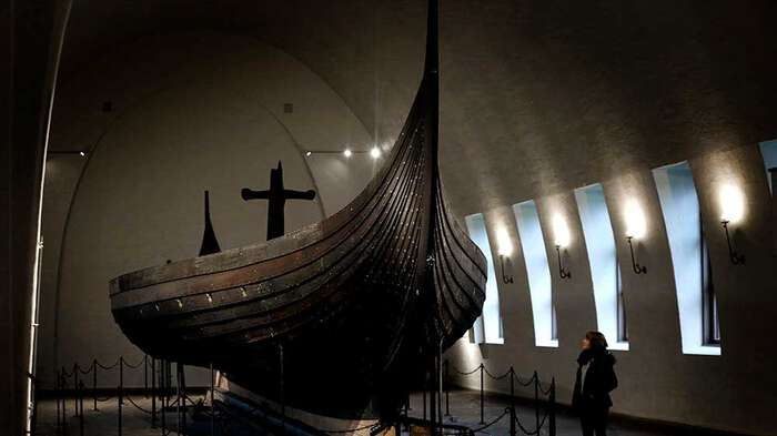 En person ser på vikingskipet Gokstadskipet da det stod i Vikingskipshuset. Dunkel belysning.