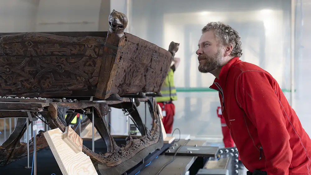 Mann inspiserer en slede fra vikingtiden.