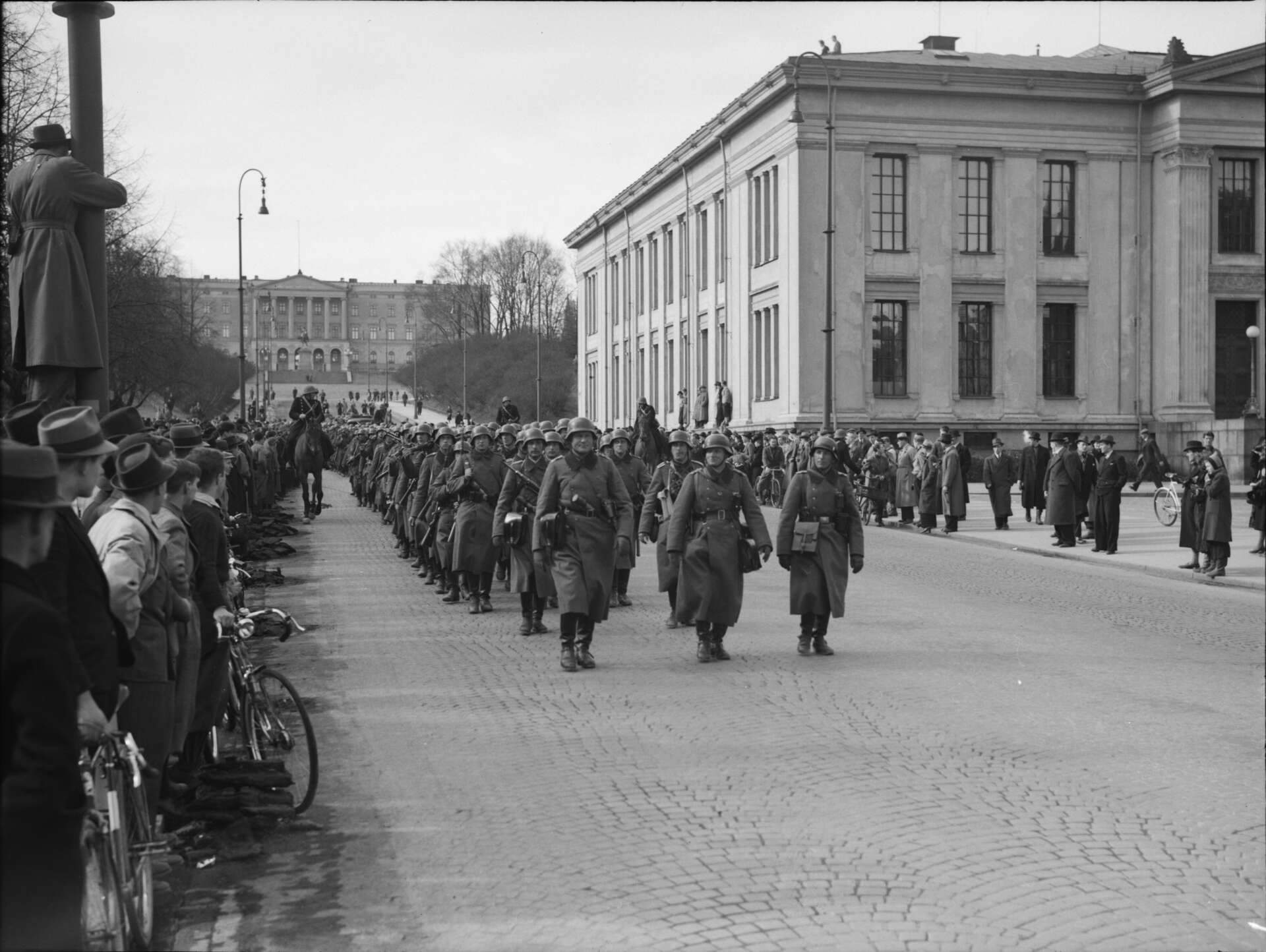 Svarthvitt bilde av Hitlers hær som marsjerer nedover Karl Johans gate i Oslo.