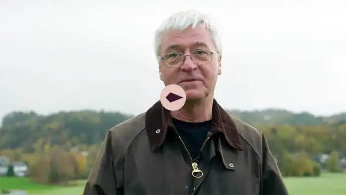 Man looking into the camera. Forest and green fields in the background.